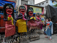 A mother and child stand beside displayed figurines of demons at a porters hub in Kolkata, India, on October 29, 2024, ahead of the Hallowee...