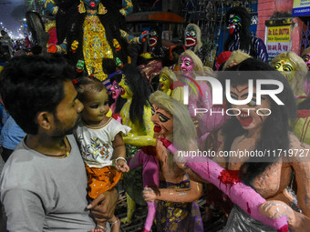 A father and child stand beside displayed figurines of demons at a porters hub in Kolkata, India, on October 29, 2024, ahead of the Hallowee...