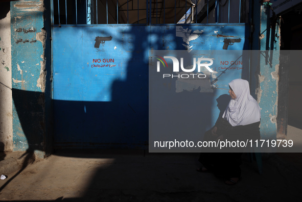 A Palestinian woman sits in front of a gate at the UNRWA (United Nations Relief and Works Agency) center at the Nuseirat refugee camp in the...