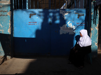 A Palestinian woman sits in front of a gate at the UNRWA (United Nations Relief and Works Agency) center at the Nuseirat refugee camp in the...