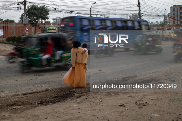 A woman waits by the roadside with her child in her lap as she looks for transport in Dhaka, Bangladesh, on October 28, 2024. 