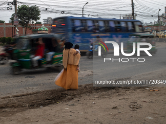 A woman waits by the roadside with her child in her lap as she looks for transport in Dhaka, Bangladesh, on October 28, 2024. (