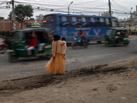 A woman waits by the roadside with her child in her lap as she looks for transport in Dhaka, Bangladesh, on October 28, 2024. (