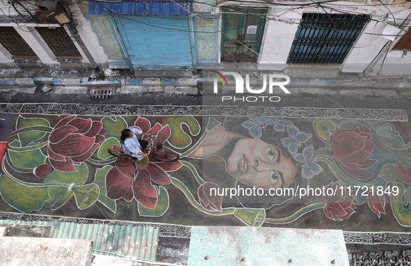 A woman rides a bicycle on the graffiti-painted road in front of a ''pandal,'' a decorated temporary platform, ahead of the Kali Puja festiv...