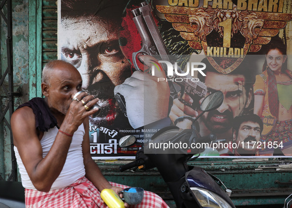 A man drinks tea in front of a poster of a Hindi movie outside a ''pandal'' (a temporary platform), a decorated structure, ahead of the Kali...