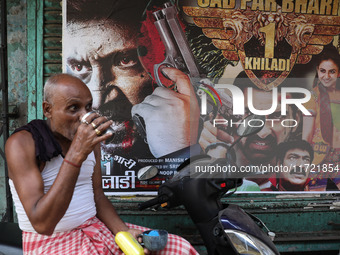 A man drinks tea in front of a poster of a Hindi movie outside a ''pandal'' (a temporary platform), a decorated structure, ahead of the Kali...