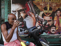 A man drinks tea in front of a poster of a Hindi movie outside a ''pandal'' (a temporary platform), a decorated structure, ahead of the Kali...