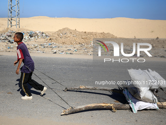 A Palestinian boy pulls sacks loaded with salvaged firewood and walks along a street in Khan Yunis, southern Gaza Strip, on October 30, 2024...