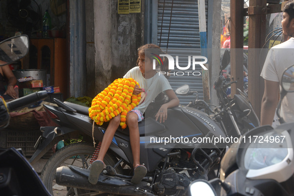 A seller's child sits on a scooter while people buy flowers from roadside sellers for home decorations on the occasion of 'Diwali,' the Hind...