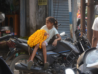 A seller's child sits on a scooter while people buy flowers from roadside sellers for home decorations on the occasion of 'Diwali,' the Hind...