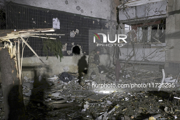 A serviceman with a torch searches the ground outside a section of a nine-story residential building destroyed by a Russian glide bomb in Kh...