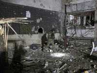 A serviceman with a torch searches the ground outside a section of a nine-story residential building destroyed by a Russian glide bomb in Kh...