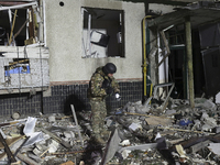 A serviceman with a torch searches the ground outside a section of a nine-story residential building destroyed by a Russian glide bomb in Kh...