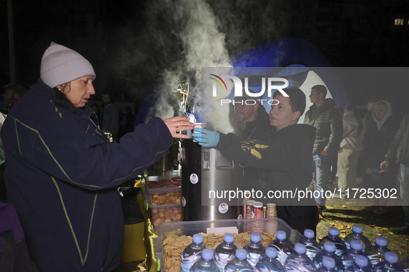 A woman receives a hot beverage at a makeshift kitchen set up outside a section of a nine-storey residential building destroyed by a Russian...