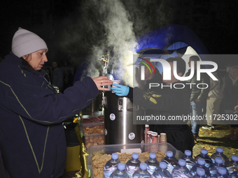 A woman receives a hot beverage at a makeshift kitchen set up outside a section of a nine-storey residential building destroyed by a Russian...