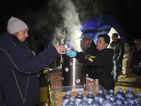 A woman receives a hot beverage at a makeshift kitchen set up outside a section of a nine-storey residential building destroyed by a Russian...