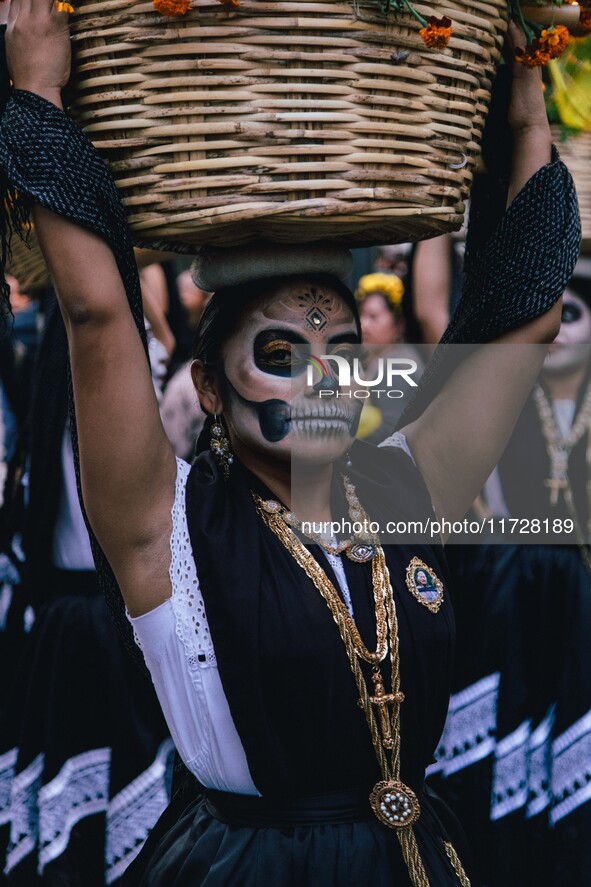 A woman wearing a traditional Mexican dress and with her face painted as a skull takes part in a parade known locally as a 'comparsa,' walki...