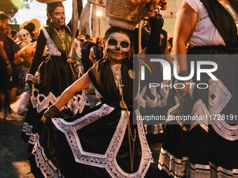 A woman wearing a traditional Mexican dress and with her face painted as a skull takes part in a parade known locally as a 'comparsa,' walki...