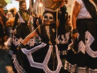 A woman wearing a traditional Mexican dress and with her face painted as a skull takes part in a parade known locally as a 'comparsa,' walki...