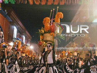 A woman wearing a traditional Mexican dress and with her face painted as a skull takes part in a parade known locally as a 'comparsa,' walki...