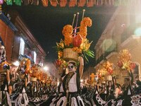 A woman wearing a traditional Mexican dress and with her face painted as a skull takes part in a parade known locally as a 'comparsa,' walki...