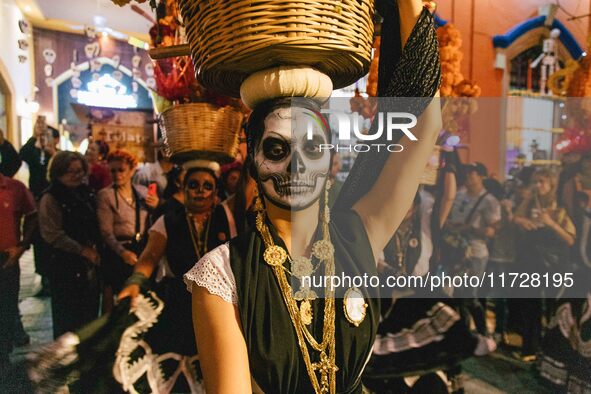 A woman wearing a traditional Mexican dress and with her face painted as a skull takes part in a parade known locally as a 'comparsa,' walki...