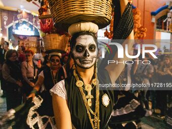 A woman wearing a traditional Mexican dress and with her face painted as a skull takes part in a parade known locally as a 'comparsa,' walki...