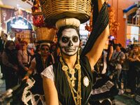 A woman wearing a traditional Mexican dress and with her face painted as a skull takes part in a parade known locally as a 'comparsa,' walki...