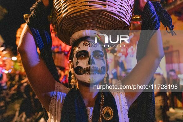 A woman wearing a traditional Mexican dress and with her face painted as a skull takes part in a parade known locally as a 'comparsa,' walki...