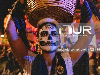 A woman wearing a traditional Mexican dress and with her face painted as a skull takes part in a parade known locally as a 'comparsa,' walki...