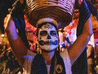 A woman wearing a traditional Mexican dress and with her face painted as a skull takes part in a parade known locally as a 'comparsa,' walki...