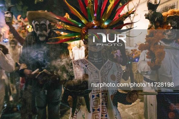 A woman wearing a traditional Mexican dress and with her face painted as a skull takes part in a parade known locally as a 'comparsa,' walki...