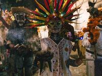 A woman wearing a traditional Mexican dress and with her face painted as a skull takes part in a parade known locally as a 'comparsa,' walki...