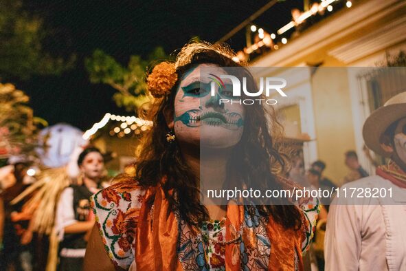 A woman wearing a traditional Mexican dress and with her face painted as a skull takes part in a parade known locally as a 'comparsa,' walki...