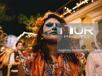 A woman wearing a traditional Mexican dress and with her face painted as a skull takes part in a parade known locally as a 'comparsa,' walki...