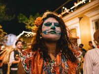 A woman wearing a traditional Mexican dress and with her face painted as a skull takes part in a parade known locally as a 'comparsa,' walki...