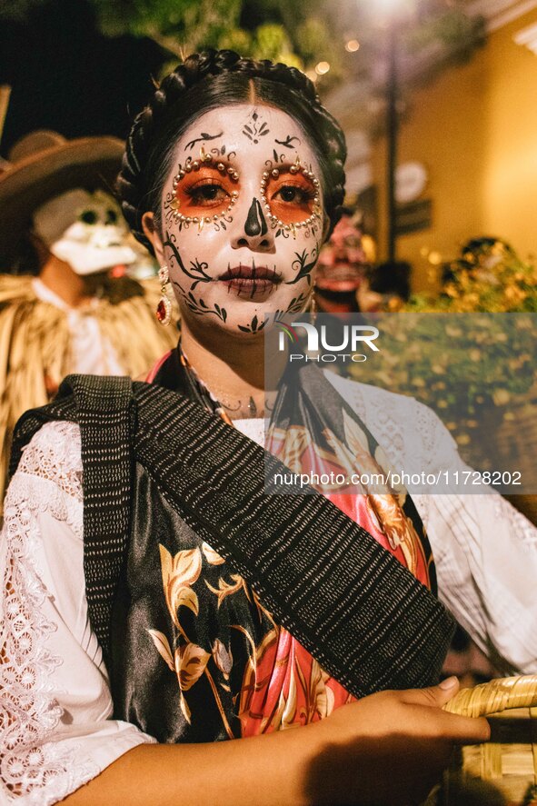 A woman wearing a traditional Mexican dress and with her face painted as a skull takes part in a parade known locally as a 'comparsa,' walki...