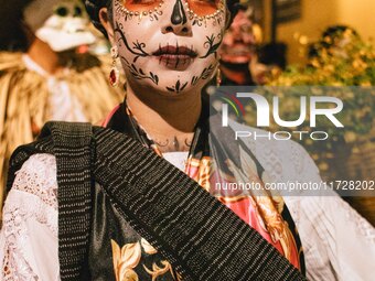 A woman wearing a traditional Mexican dress and with her face painted as a skull takes part in a parade known locally as a 'comparsa,' walki...