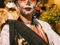 A woman wearing a traditional Mexican dress and with her face painted as a skull takes part in a parade known locally as a 'comparsa,' walki...