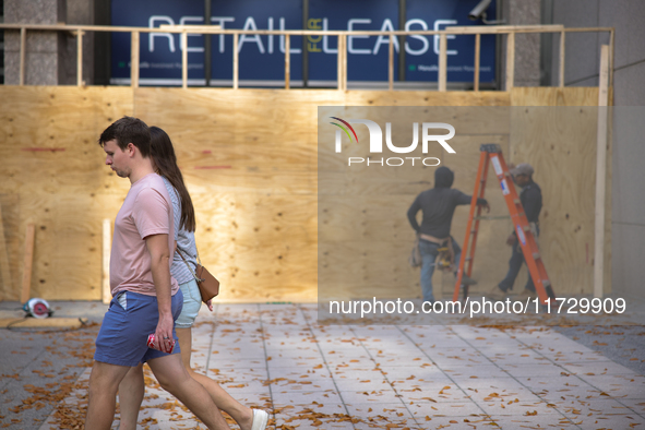 People walk past boarded up storefronts near the White House in Washington, D.C. on November 1, 2024 as local busineses prepare for possible...