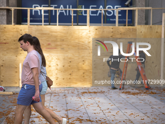 People walk past boarded up storefronts near the White House in Washington, D.C. on November 1, 2024 as local busineses prepare for possible...