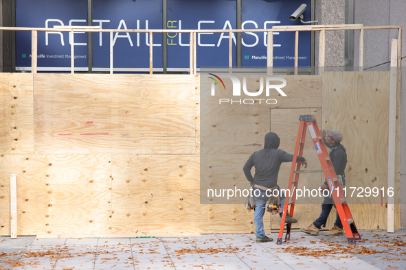 Workers cover storefront entrances with plywood near the White House in Washington, D.C. on November 1, 2024 in preparation for possible civ...