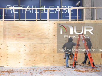 Workers cover storefront entrances with plywood near the White House in Washington, D.C. on November 1, 2024 in preparation for possible civ...