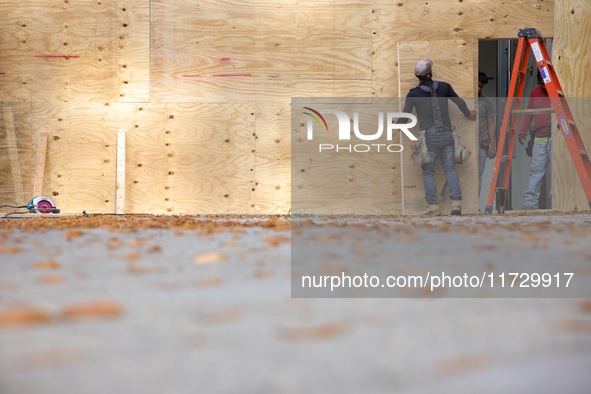 Workers cover storefront entrances with plywood near the White House in Washington, D.C. on November 1, 2024 in preparation for possible civ...