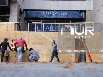 Workers cover storefront entrances with plywood near the White House in Washington, D.C. on November 1, 2024 in preparation for possible civ...