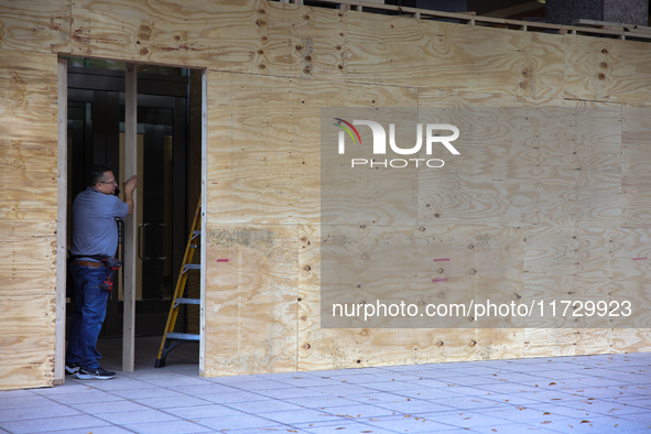 Workers cover storefront entrances with plywood near the White House in Washington, D.C. on November 1, 2024 in preparation for possible civ...