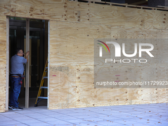 Workers cover storefront entrances with plywood near the White House in Washington, D.C. on November 1, 2024 in preparation for possible civ...