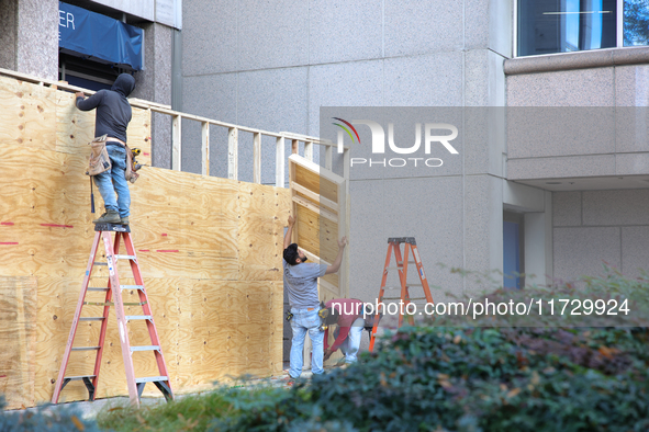 Workers cover storefront entrances with plywood near the White House in Washington, D.C. on November 1, 2024 in preparation for possible civ...