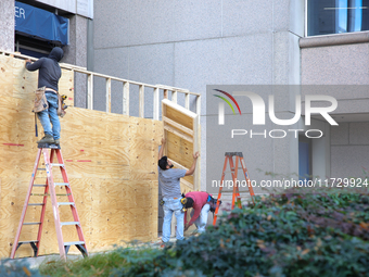 Workers cover storefront entrances with plywood near the White House in Washington, D.C. on November 1, 2024 in preparation for possible civ...