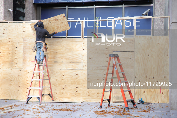 Workers cover storefront entrances with plywood near the White House in Washington, D.C. on November 1, 2024 in preparation for possible civ...